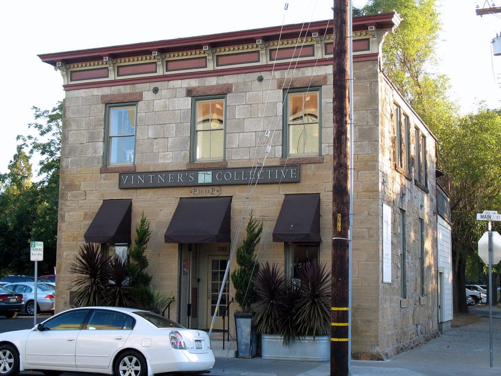 Historic stone building with a sign for Vintner's Collective and a white car parked outside.